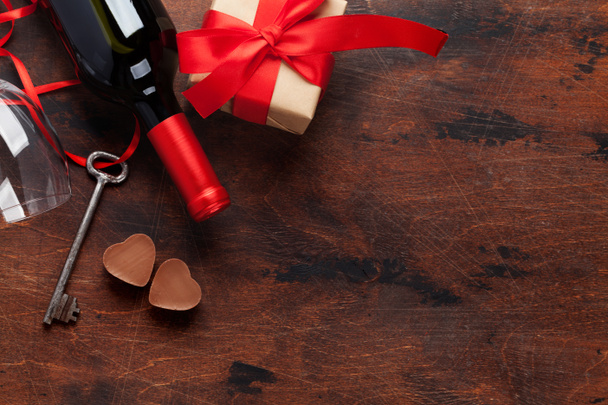 Valentines day greeting card with wine bottle, chocolate hearts, key and gift box on wooden background. Top view with space for your greetings. Flat lay - Photo, Image