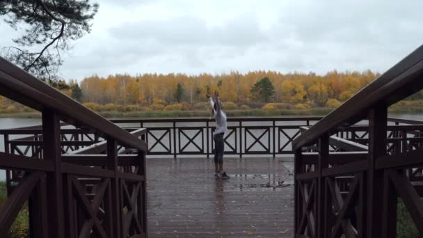 Sportowy kobieta rozgrzewa się przed jogging na drewnianym molo. - Materiał filmowy, wideo