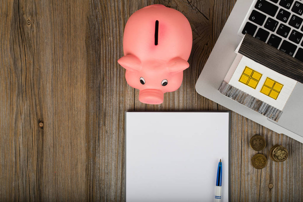 Blank sheet of paper and pink piggy bank close to the laptop. Closeup - Foto, Imagen