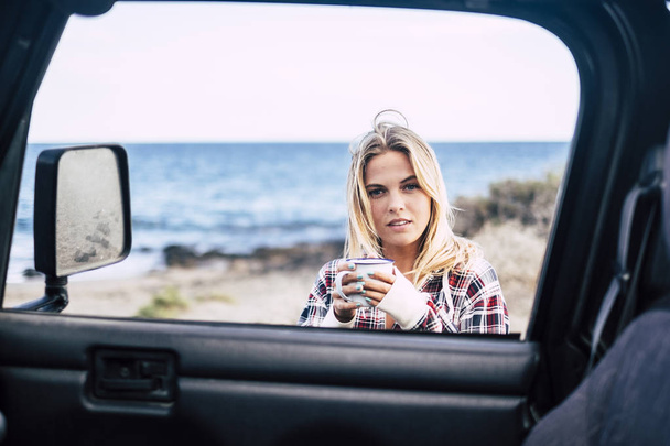 Attractive young millennial blonde take a break outside of her off road car while travel and discover the world - Photo, Image