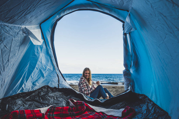 Menina loira alegre bonita sorrindo visto de dentro de uma tenda acampada na praia diretamente na areia - Foto, Imagem