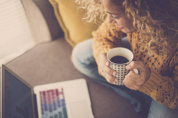 mulher com cabelo encaracolado e xícara de café trabalhando com computador portátil em casa
 - Foto, Imagem
