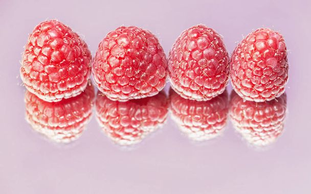 Four bright raspberries on a mirror form their double ,studio shot , funny effect - Fotó, kép