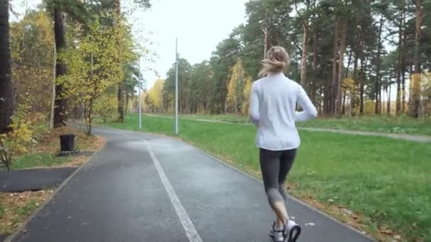Rückansicht einer jungen blonden Frau, die im Herbstpark läuft. - Filmmaterial, Video