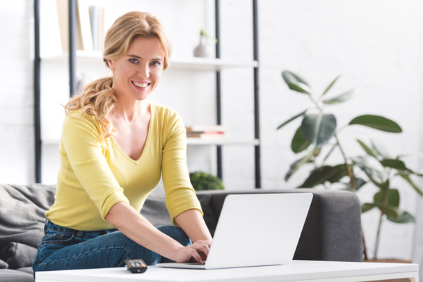 houkutteleva nainen käyttää kannettavaa tietokonetta ja hymyilee kameran kotona
 - Valokuva, kuva