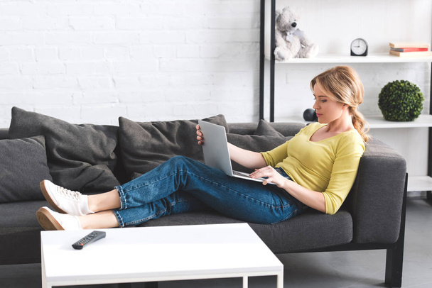 side view of beautiful woman using laptop on couch - Fotografie, Obrázek