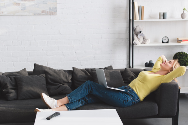side view of happy relaxed woman lying with laptop on couch - Foto, imagen