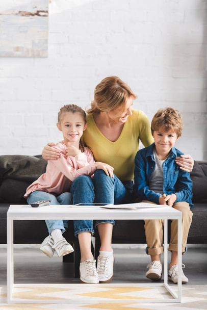happy mother looking at adorable smiling kids sitting together on couch - Φωτογραφία, εικόνα