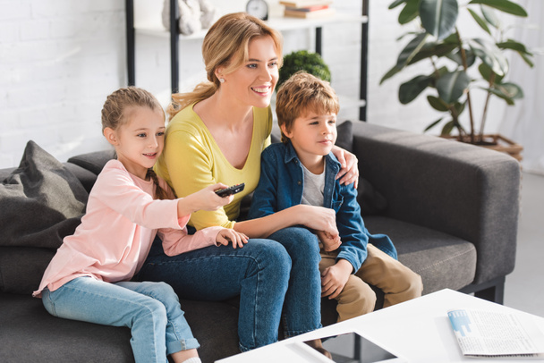 felice madre e simpatici bambini sorridenti utilizzando il telecomando e guardando la TV insieme
  - Foto, immagini