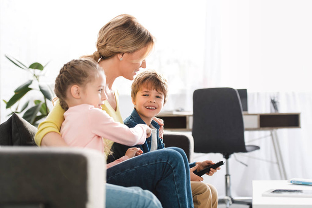 Gelukkig moeder met schattige kinderen tv kijken samen thuis - Foto, afbeelding