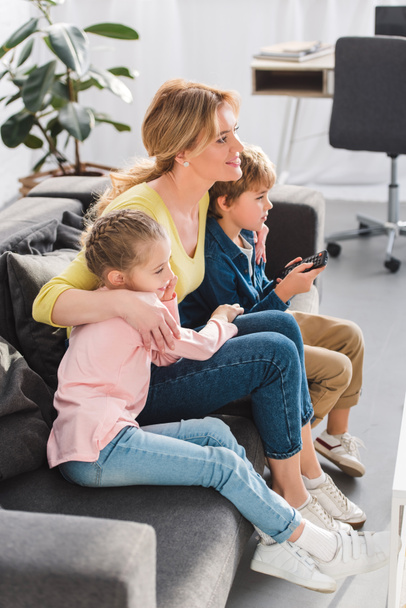 high angle view of mother and kids with remote controller sitting in sofa and watching tv - Fotografie, Obrázek