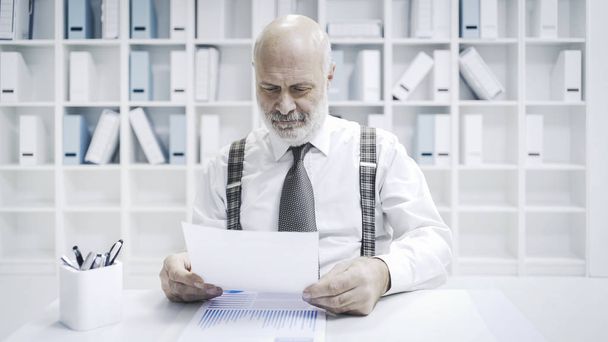 Professional senior businessman working in the office, he is checking paperwork and financial reports - 写真・画像