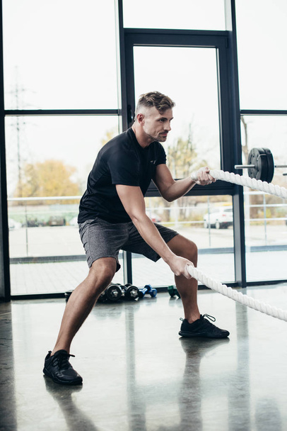 boční pohled pohledný sportovec cvičit s provazy v tělocvičně  - Fotografie, Obrázek