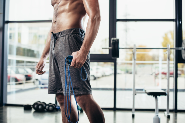 mid section of shirtless sportsman holding skipping rope in gym  - Photo, Image