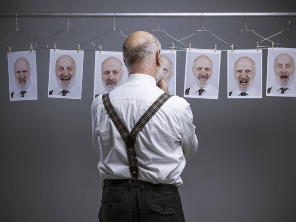 Mature businessman staring at his multiple personalities and expressions on a collection of hanging portraits: mind self analysis and emotions concept - Photo, image