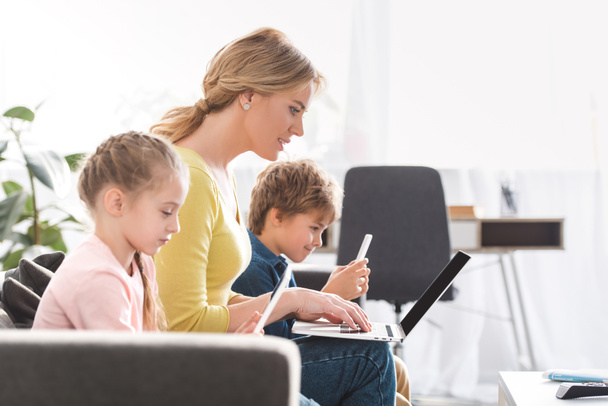 side view of mother with adorable children using digital devices at home  - Photo, Image