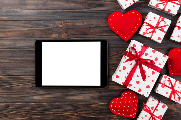 digitaler Tablet-Bildschirm mit Geschenkbox und Herzdekor auf Holztisch. Ansicht von oben. Valentinstag Konzept Hintergrund. - Foto, Bild