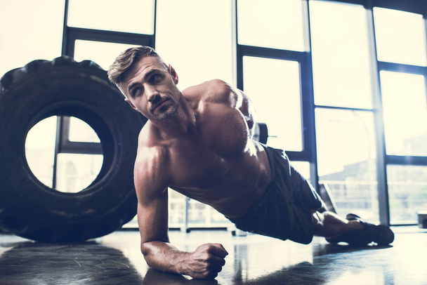 apuesto deportista sin camisa haciendo tablón en una mano en el gimnasio
  - Foto, imagen