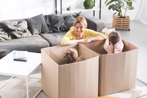 high angle view of happy mother looking at cute little children playing in cardboard boxes  - Photo, Image