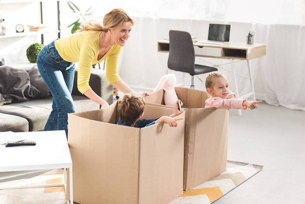 happy mother playing with kids sitting in cardboard boxes at home - Φωτογραφία, εικόνα