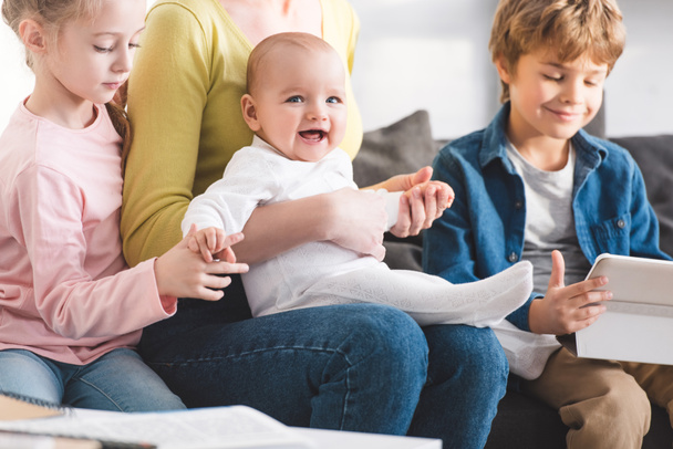 Schnappschuss von Mutter mit Kleinkind und niedlichen Geschwistern, die zusammen auf Sofa sitzen - Foto, Bild