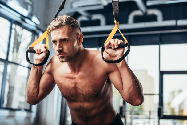 handsome shirtless sportsman working out with resistance bands in gym  - Foto, immagini