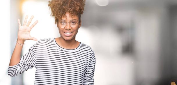 Όμορφη νεαρή αφρικανική αμερικανική γυναίκα φοράει γυαλιά πέρα από το απομονωμένο υπόβαθρο δείχνει και δείχνει προς τα επάνω με τα δάχτυλα αριθμός πέντε ενώ χαμογελώντας αυτοπεποίθηση και χαρούμενοι. - Φωτογραφία, εικόνα