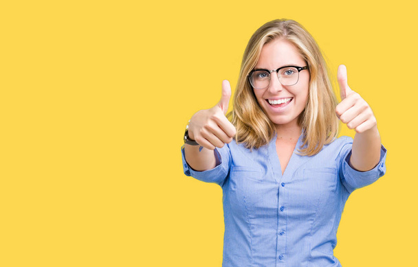 Beautiful young business woman over isolated background approving doing positive gesture with hand, thumbs up smiling and happy for success. Looking at the camera, winner gesture. - Photo, Image
