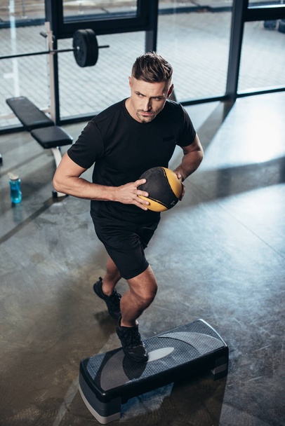 high angle view of handsome sportsman training on step platform with medicine ball in gym - Fotoğraf, Görsel