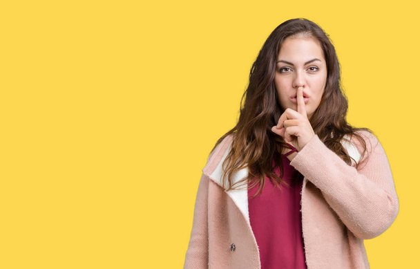 Beautiful plus size young woman wearing winter coat over isolated background asking to be quiet with finger on lips. Silence and secret concept. - Fotografie, Obrázek