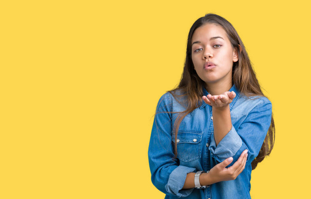 Young beautiful brunette woman wearing blue denim shirt over isolated background looking at the camera blowing a kiss with hand on air being lovely and sexy. Love expression. - Photo, Image