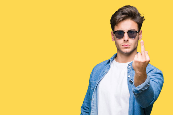 Young handsome man wearing sunglasses over isolated background Showing middle finger, impolite and rude fuck off expression - Photo, Image