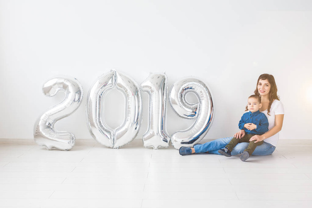 New 2019 Year is coming concept - Mother with her baby son sitting near silver colored numbers indoors. - Foto, afbeelding