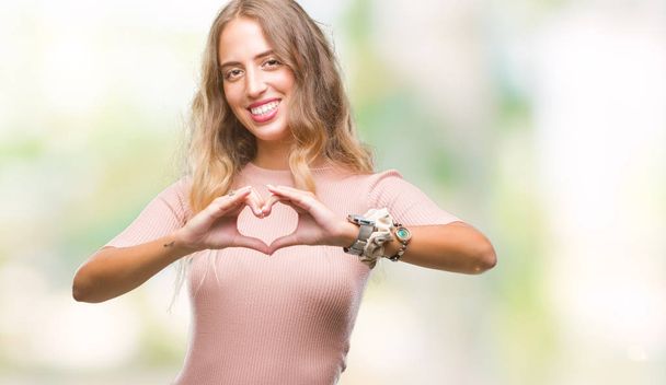 Beautiful young blonde woman over isolated background smiling in love showing heart symbol and shape with hands. Romantic concept. - Foto, afbeelding