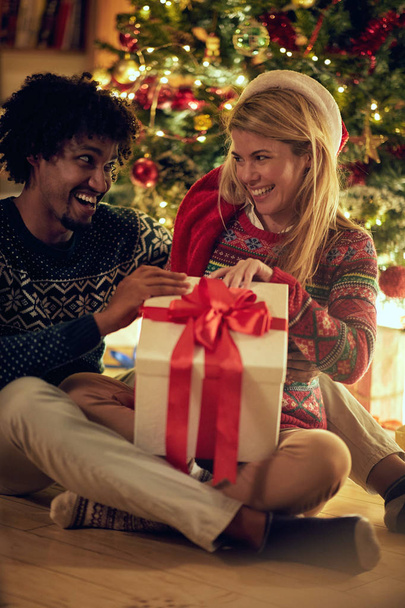Cheerful male and female exchanging Christmas presents and having fun - Fotó, kép