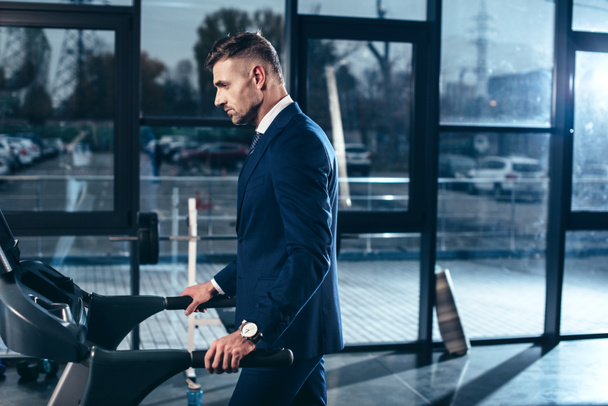 side view of handsome businessman in suit exercising on treadmill in gym - Fotografie, Obrázek