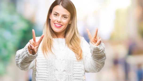 Young beautiful woman casual white sweater over isolated background smiling looking to the camera showing fingers doing victory sign. Number two. - Foto, Imagen