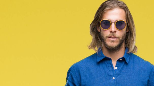 Young handsome man with long hair wearing sunglasses over isolated background with serious expression on face. Simple and natural looking at the camera. - Photo, Image