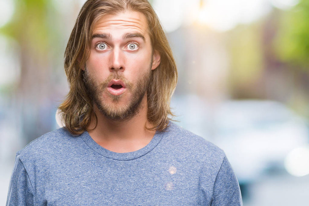 Young handsome man with long hair over isolated background afraid and shocked with surprise expression, fear and excited face. - Foto, immagini