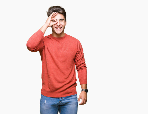 Young handsome man over isolated background doing ok gesture with hand smiling, eye looking through fingers with happy face. - Foto, Bild