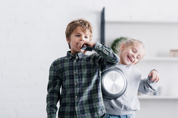 adorable siblings playing with remote controller and frying pan at home - Photo, image