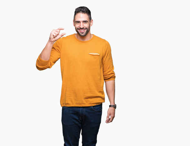 Jonge knappe man over geïsoleerde achtergrond glimlachend en vertrouwen gebaren met hand grootte teken met vingers doen tijdens het kijken en de camera. Maatregel concept. - Foto, afbeelding