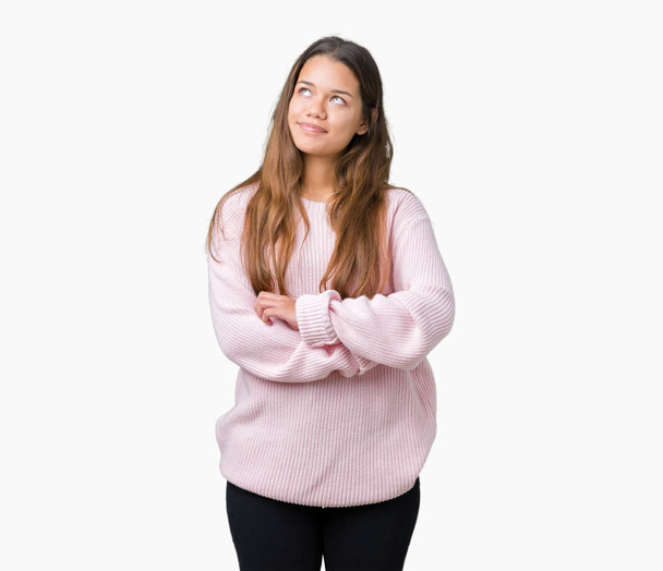 Jonge mooie brunette vrouw roze winter trui dragen over geïsoleerde achtergrond glimlachend uitziende kant en staren weg denken. - Foto, afbeelding