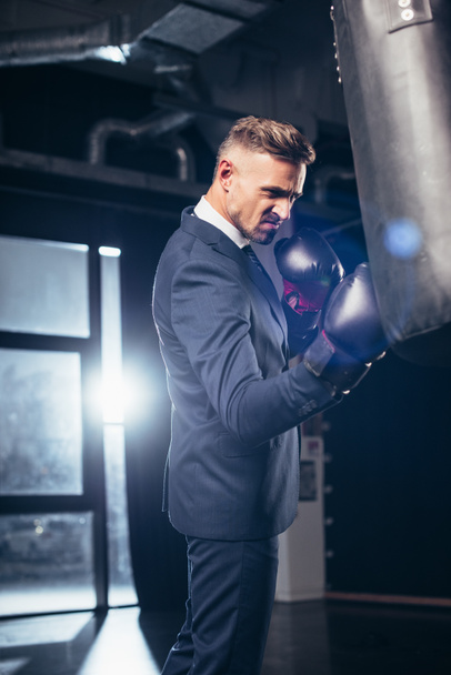 handsome businessman in suit grimacing while boxing in gym - Photo, Image