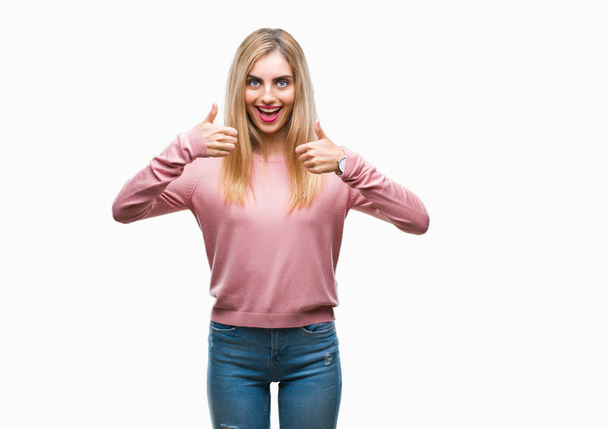 Mladá krásná blondýna žena nosí růžové zimní svetr přes znamení úspěchu izolované pozadí dělá pozitivní gesto rukou, palec se usmívá a šťastný. Při pohledu na fotoaparát s veselým výrazem, vítěz gesto. - Fotografie, Obrázek