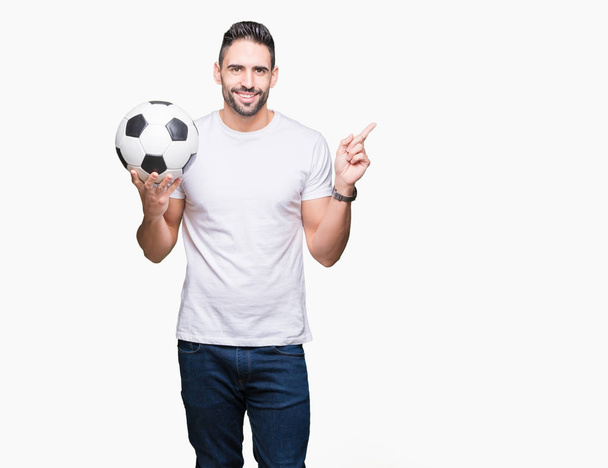 Giovane uomo che tiene palla da calcio su sfondo isolato molto felice che punta con mano e dito al lato
 - Foto, immagini