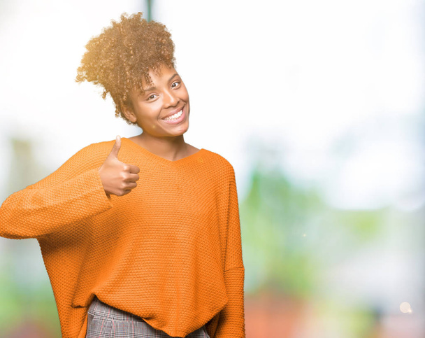 Beautiful young african american woman over isolated background doing happy thumbs up gesture with hand. Approving expression looking at the camera with showing success. - Фото, изображение