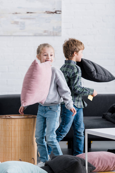 adorable siblings fighting with pillows and having fun at home  - Zdjęcie, obraz