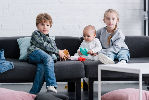 suloiset sisarukset ja pikkulapsi istuvat yhdessä sohvalla
 - Valokuva, kuva