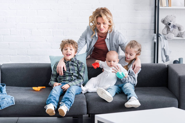 glückliche Mutter sieht drei entzückende Kinder auf der Couch sitzen - Foto, Bild
